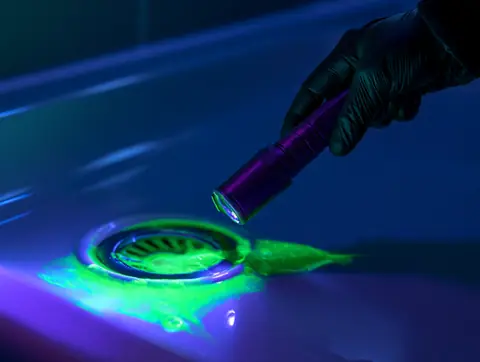 Fluorescéine verte révélée par une lampe UV autour d'une bonde de douche